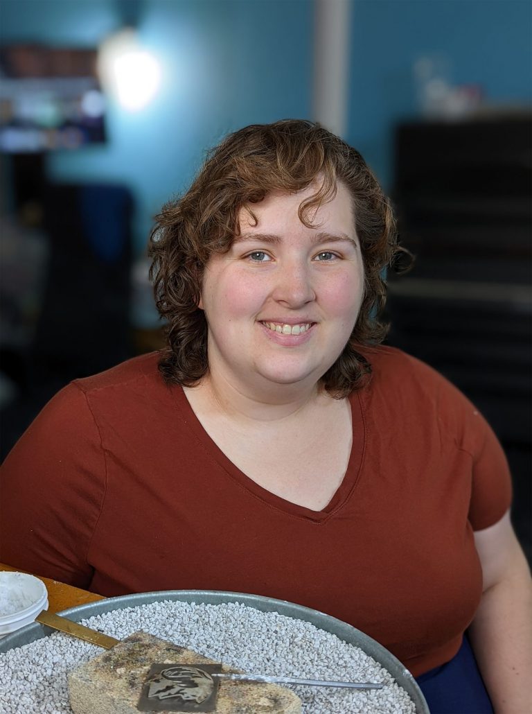 Danielle sitting at a wooden desk, with a soldering pan in front of her.
