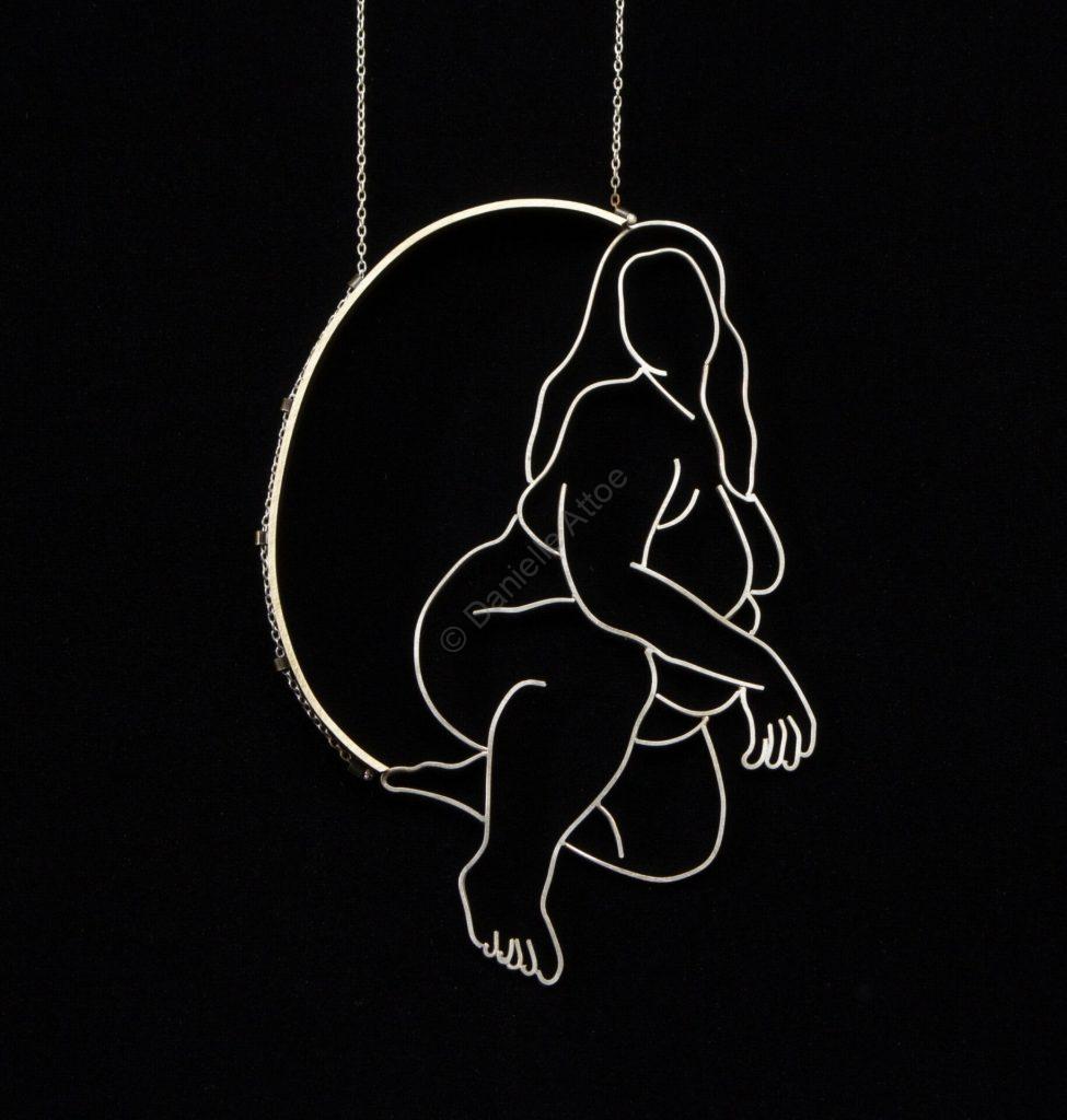 a pendant of a nude woman on one knee looking at the viewer